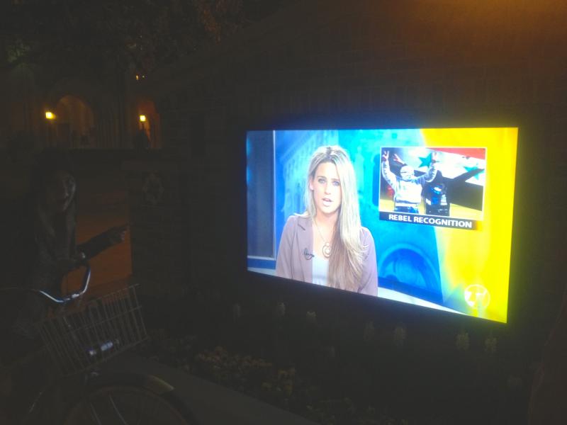 The newscast playing on the big TV on campus. 